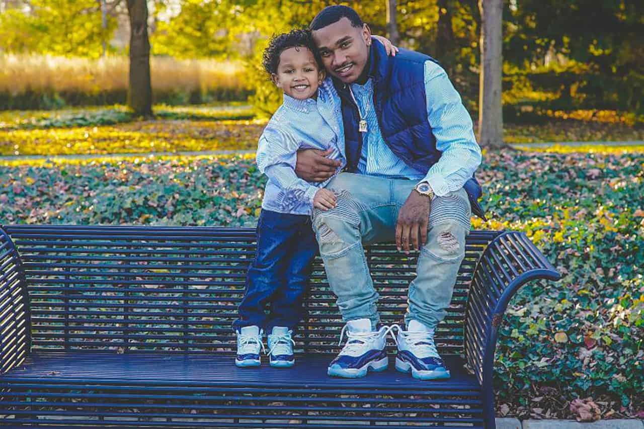 A man sitting on a bench with his son and smiling at the camera.