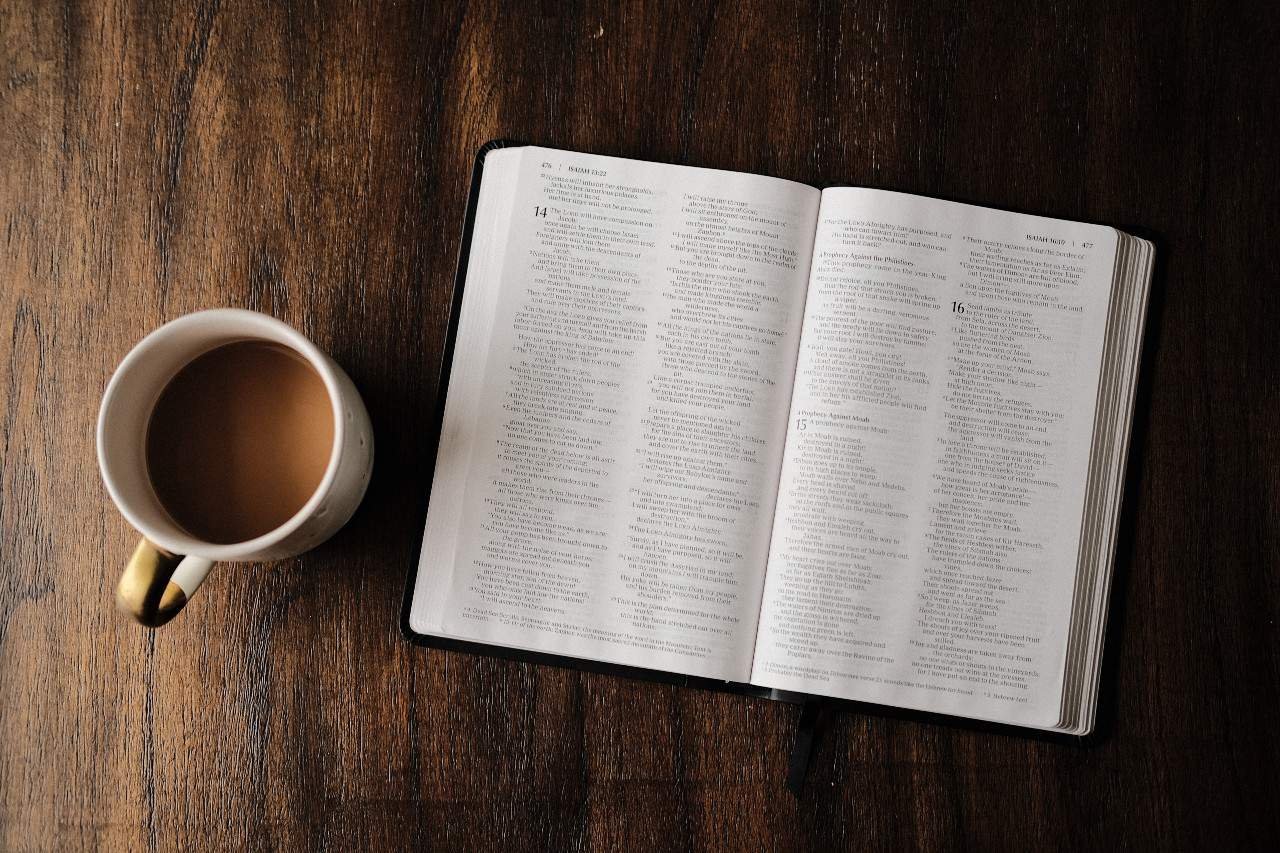 A cup of coffee next to an open Bible.