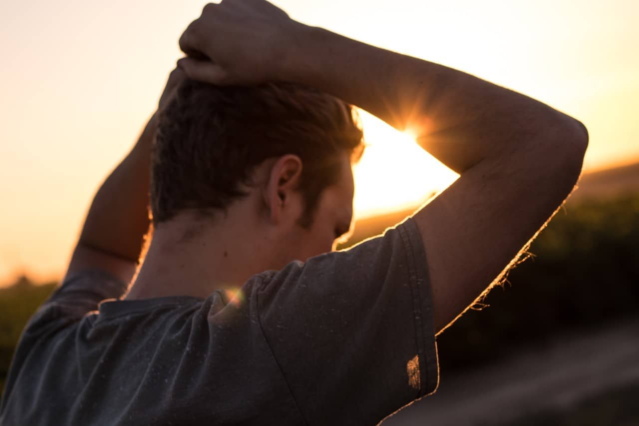 A man outside with his hands on his head at sunset.