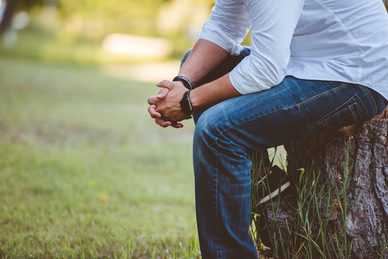 A man sitting on a tree stump with folded hands.