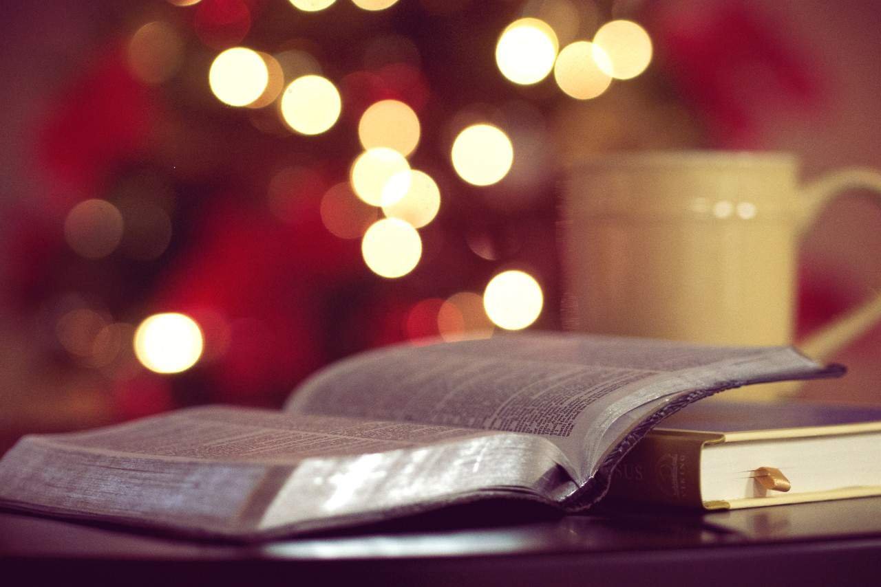 An open Bible with a cup of coffee and a lit Christmas tree in the background.