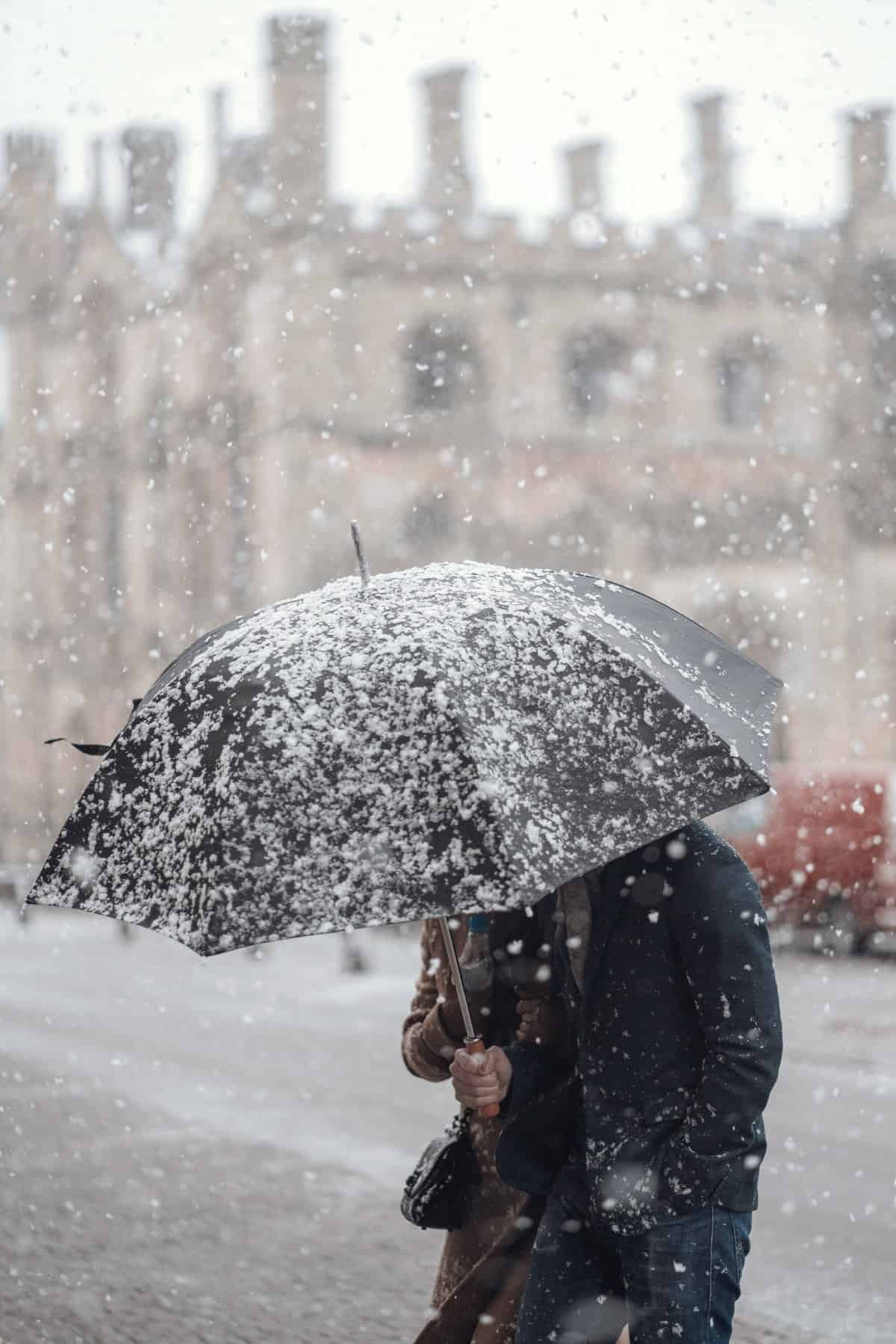 An image of a man holding an umbrella during a snow storm.
