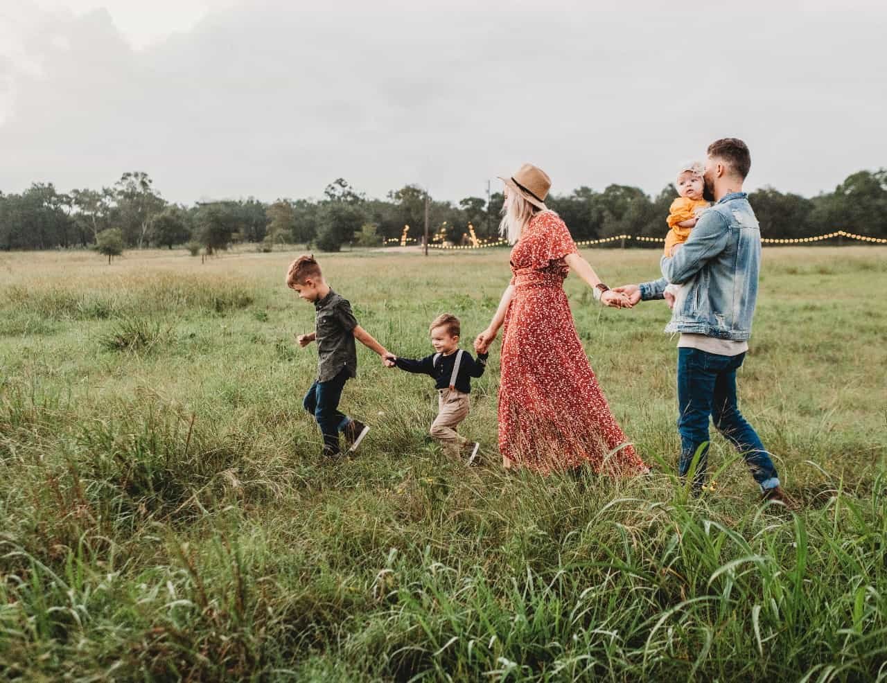 A family of five walking through a field holding hands.