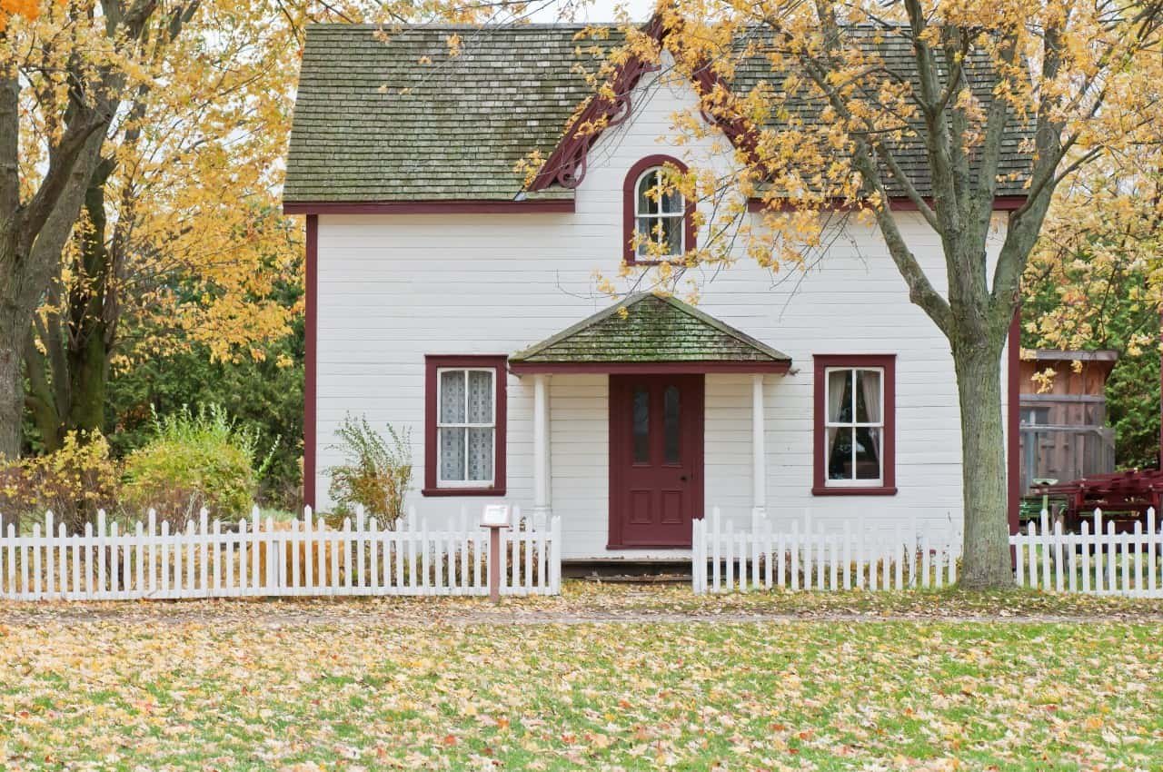 A white house with red trim with fall leaves and trees.