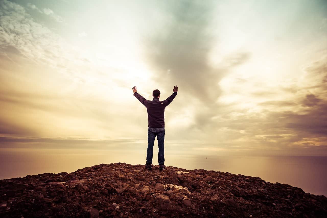 A man overlooking water with his hands raised.
