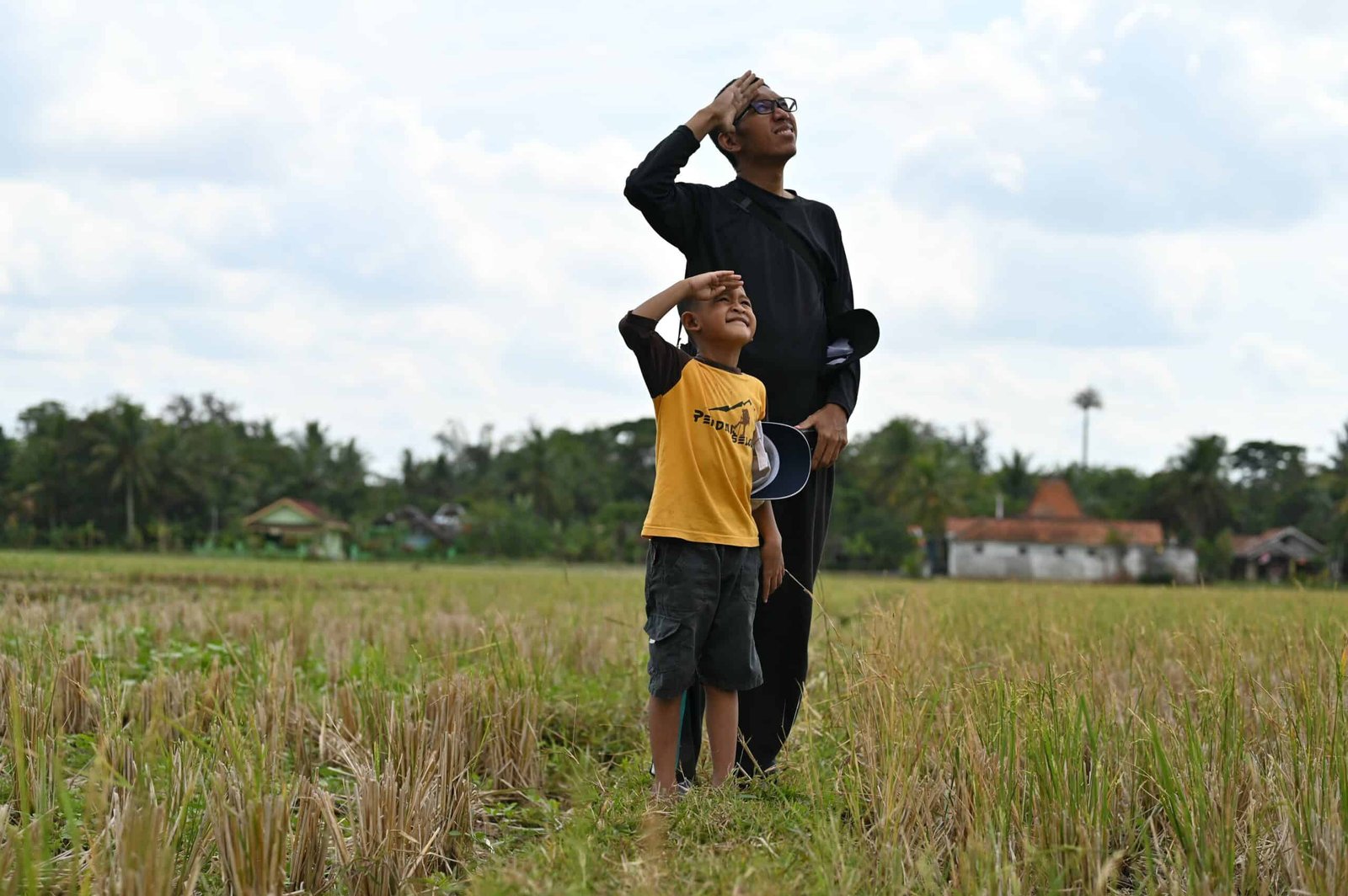 Father and son looking toward sky with right hand raised like a salute